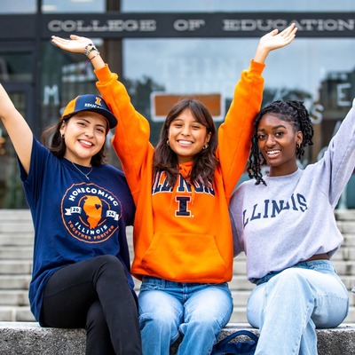 Three students with their arms raised and smiling