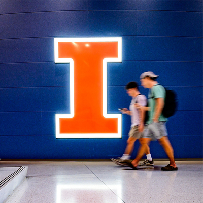 students walk by a lighted block I logo