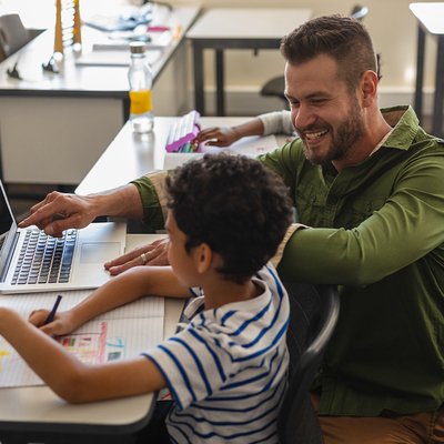 Young school teacher helping boy with study on laptop in school