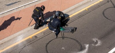 No caption on Shutterstock image. Police in riot gear kneel on or near a man laying on the pavement somewhere