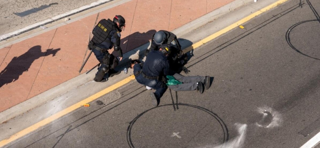 No caption on Shutterstock image. Police in riot gear kneel on or near a man laying on the pavement somewhere