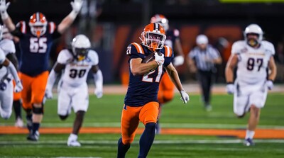 an Illini player runs with the ball while another signals in anticipation of a touchdown.