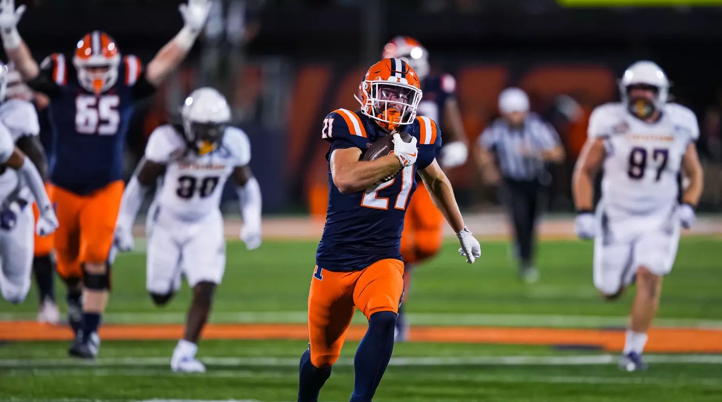 an Illini player runs with the ball while another signals in anticipation of a touchdown.