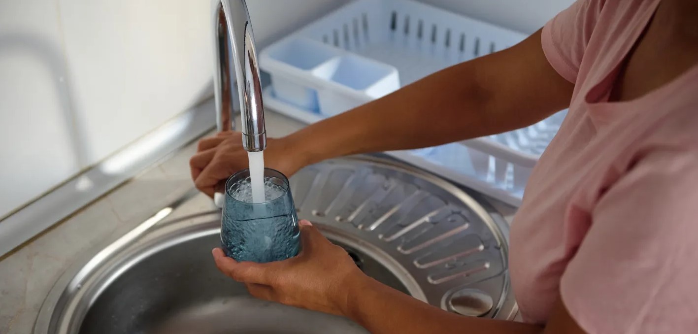 stock image of woman drawing a glass of water from a kitchen faucet. Photo from iStock