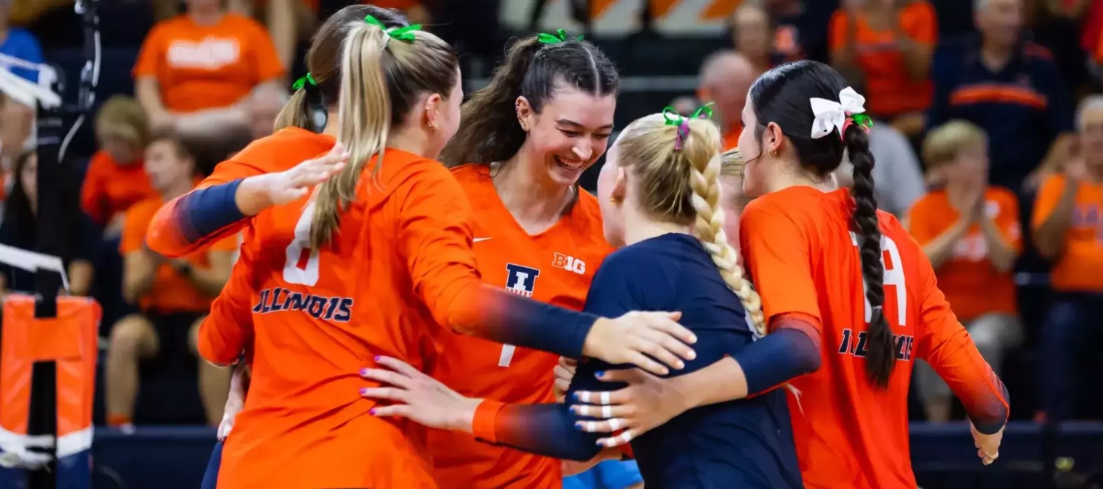 Volleyball teammates huddle, embrace and smile during a home game