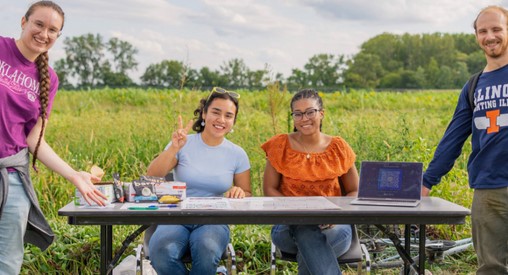 happy students sit at an information table at the Student Sustainable Farm