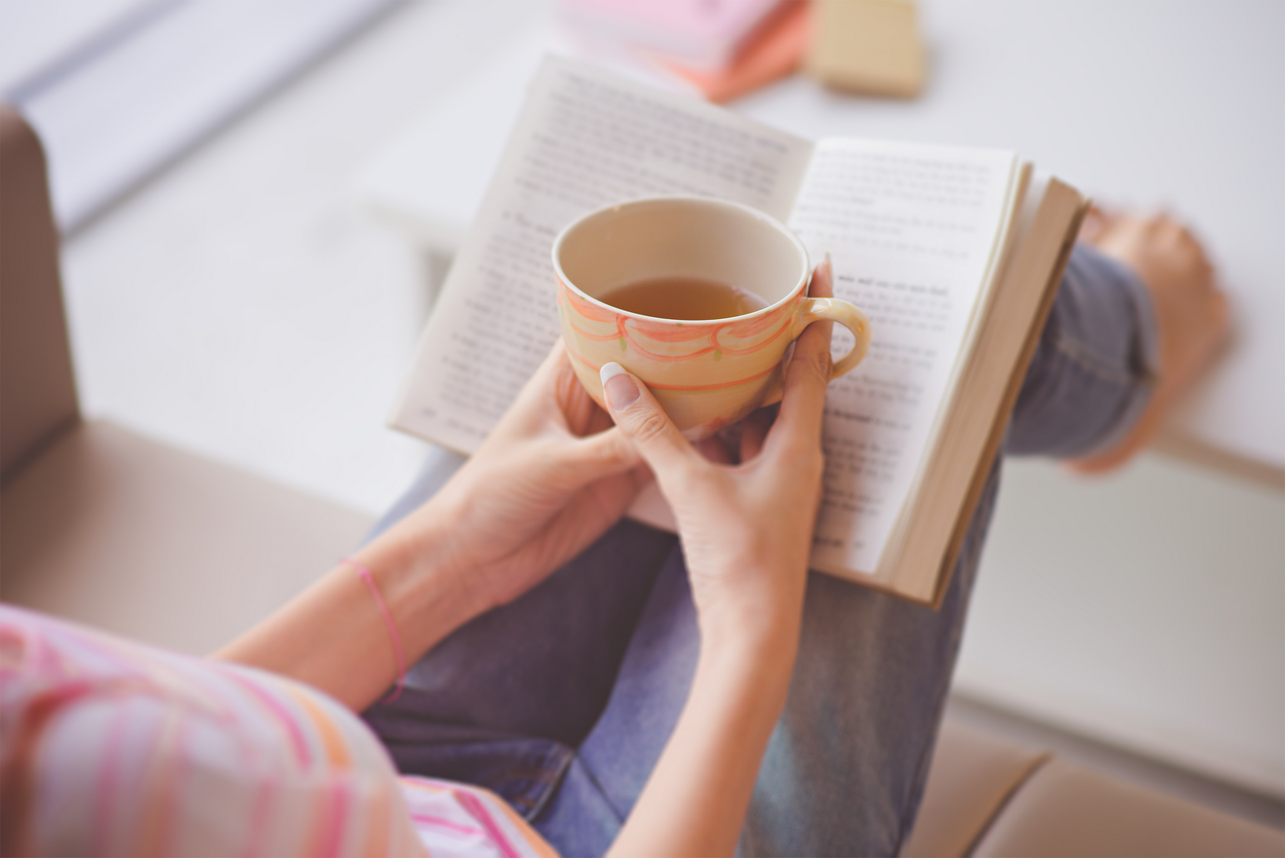 Barefoot person reading a book with a cup of tea