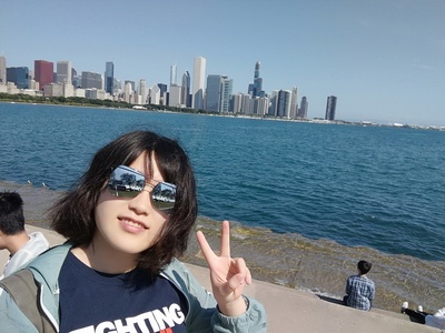 Jiayi Li makes a peace sign in front of Lake Michigan with the Chicago skyline in the background