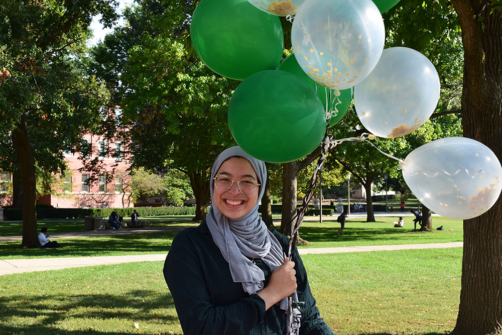 Doha Amer stands on the University of Illinois Quad holding green and white balloons