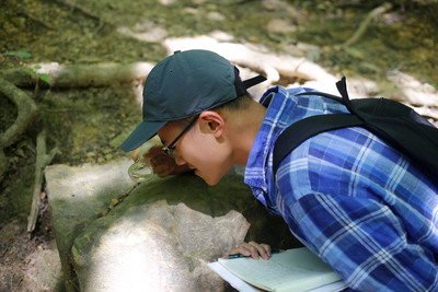 Cheelan Bo-Linn uses a magnifying glass to look at something in a rock