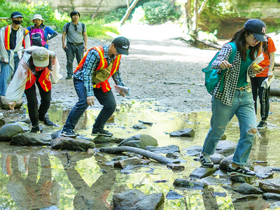 Zhejian University summer school students, wearing safet vest and backpacks, crossing a stream outside