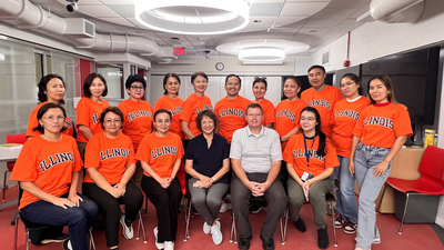 Fifteen Bolashak Scholars pose for a photo wearing orange Illinois shirts.