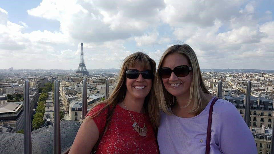Melissa Belcher stands with a friend on a rooftop terrace in Paris with the Eiffel Tower behind her