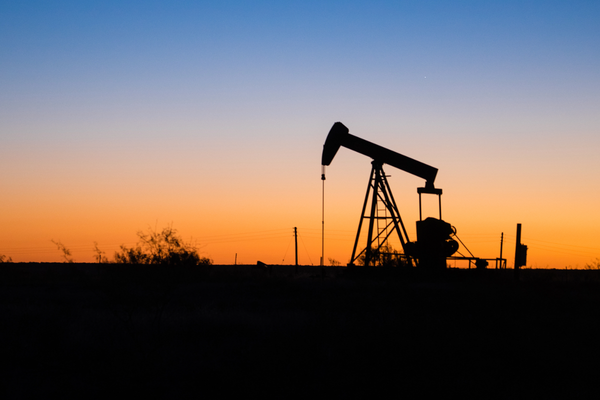 An oil pump jack on the horizon silhouetted by a setting sun.