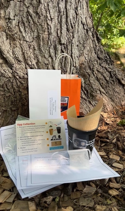 The contents of a Mosquito Ambassador Program kit, including instructions, a cup for collecting mosquito eggs, and an envelope for mailing collected eggs.