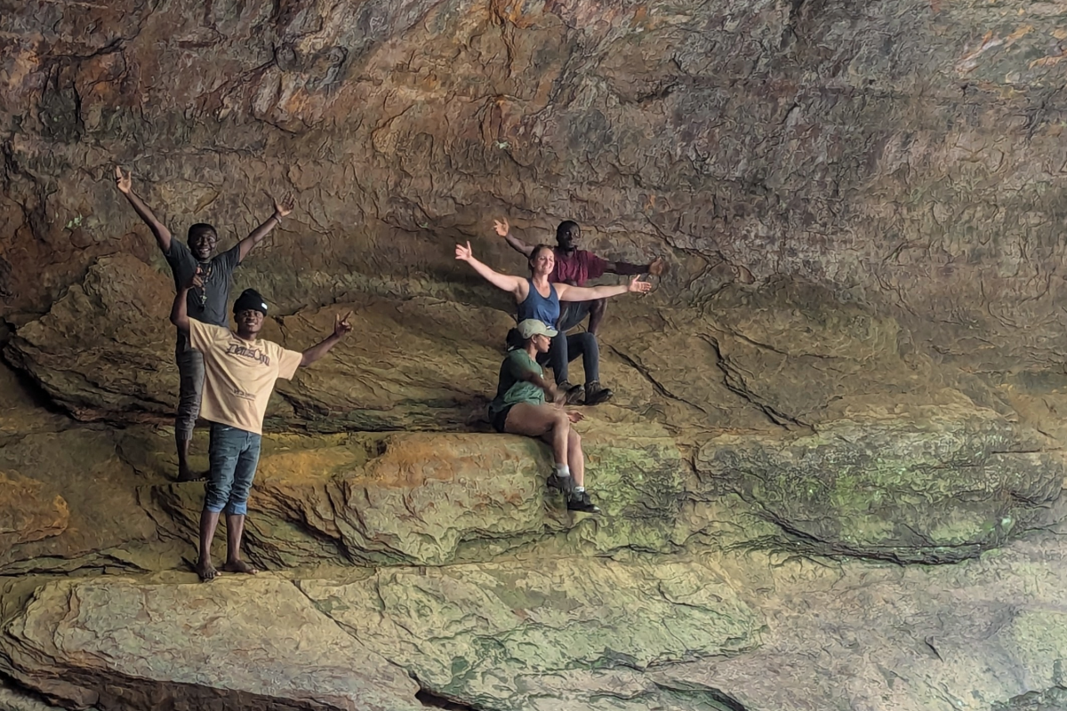 Four students standing beneath a sandstone formation.