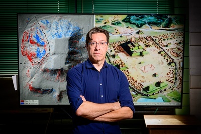 Andrew White poses in front of screens showing maps of Illinois cultural sites.