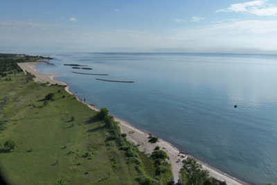 Aerial view of the Lake Michigan coast on a summer day with green inland vegetation, a sandy shore, and clear blue water.