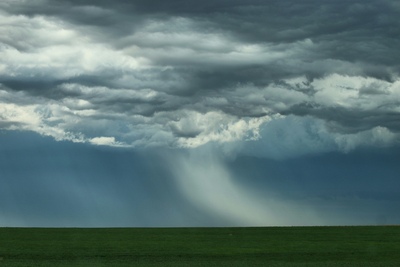 Heavy rain falls from storm clouds over fields.
