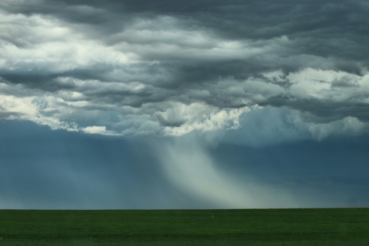 Heavy rain falls from storm clouds over fields.