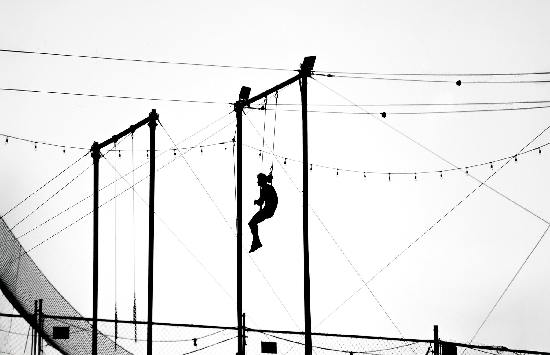 Silhouette of a trapeze artist swinging high above.