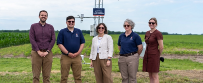 Five people standing in front of the monitoring station in a field.