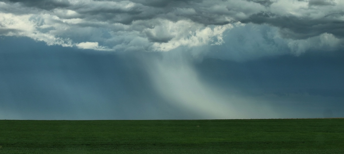 Heavy rain falls from storm clouds over fields.