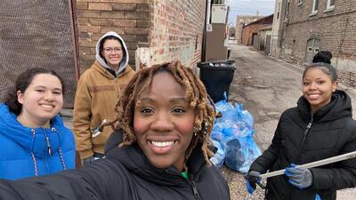 Selfie of Brianna Brianna Guerrier standing in front of buildings with three other students smiling and posing in the background