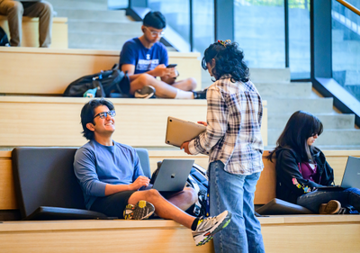 two students are talking in a large room with staircase-like desks