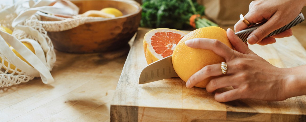 a woman's hands using a knife to cut a grapefruit on a cutting board