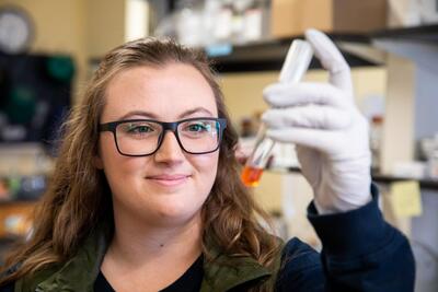 A woman holds a test tube close to her face and smiles in a lab