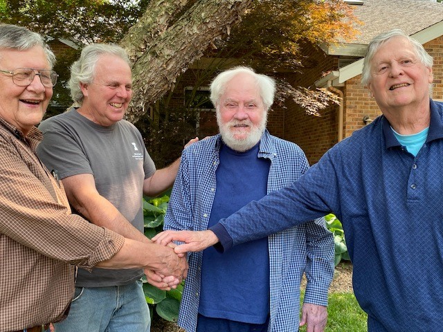 4 men clasp hands, standing outside.