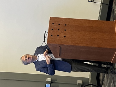 A gray-haired man in a dark blue blazer standing behind a wooden podium.
