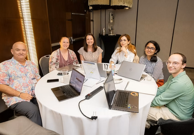 six people seated at a table with laptops open