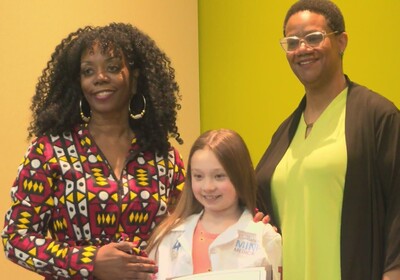 Two adults smile while posing with a child wearing a white lab coat