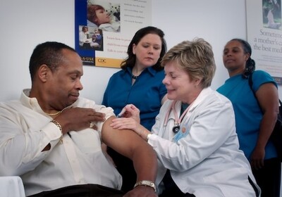 A doctor administers an injection to a patient while two nurses look on