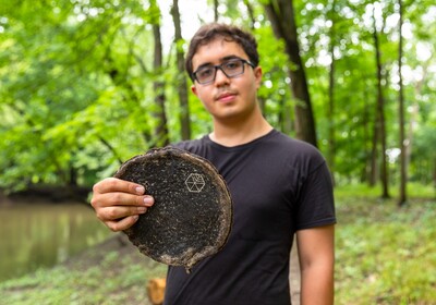 Gabe Tavas holding a piece of wood in a forest