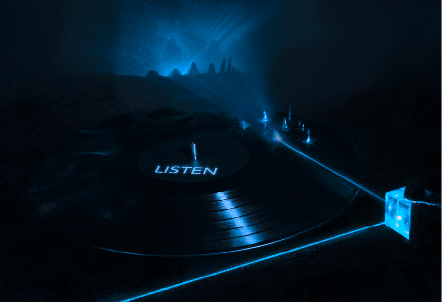LISTEN. Dark scene with a vinyl record labeled LISTEN. A blue laser beam skims its rippled surface and casts a wave-like shadow.