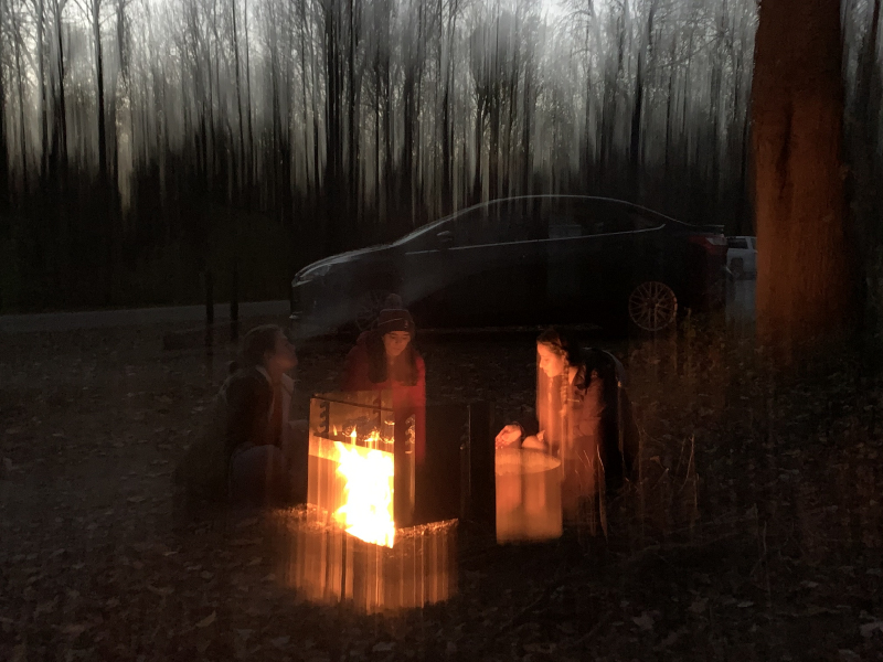 In Light of Ourselves. Three friends sitting around a campfire. Streaks of light move up and down the image vertically, warping their faces.