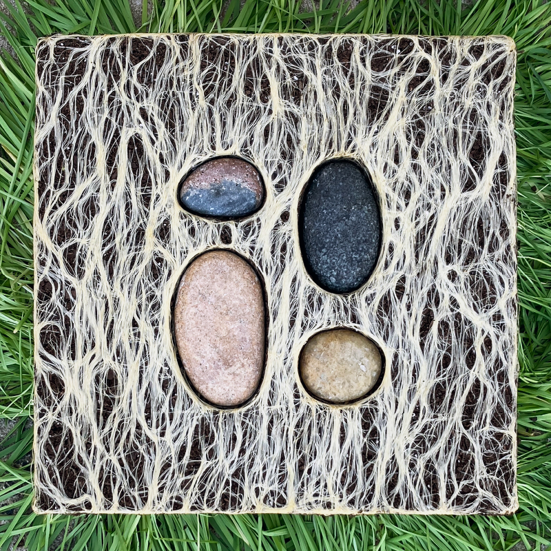 Ambiguity and Affect. A cube-like sculpture made from dirt, plant roots, and inverted green grass holds four smooth stones.